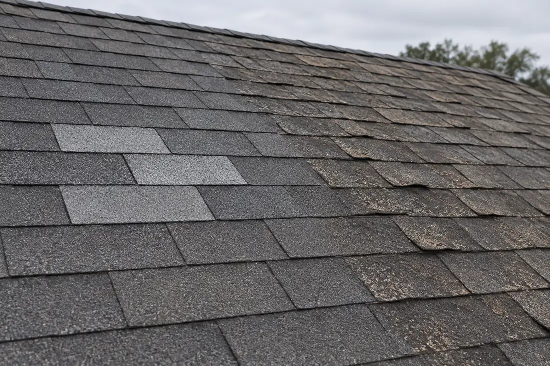 Illustrative roof with patched shingles beside older curling shingles